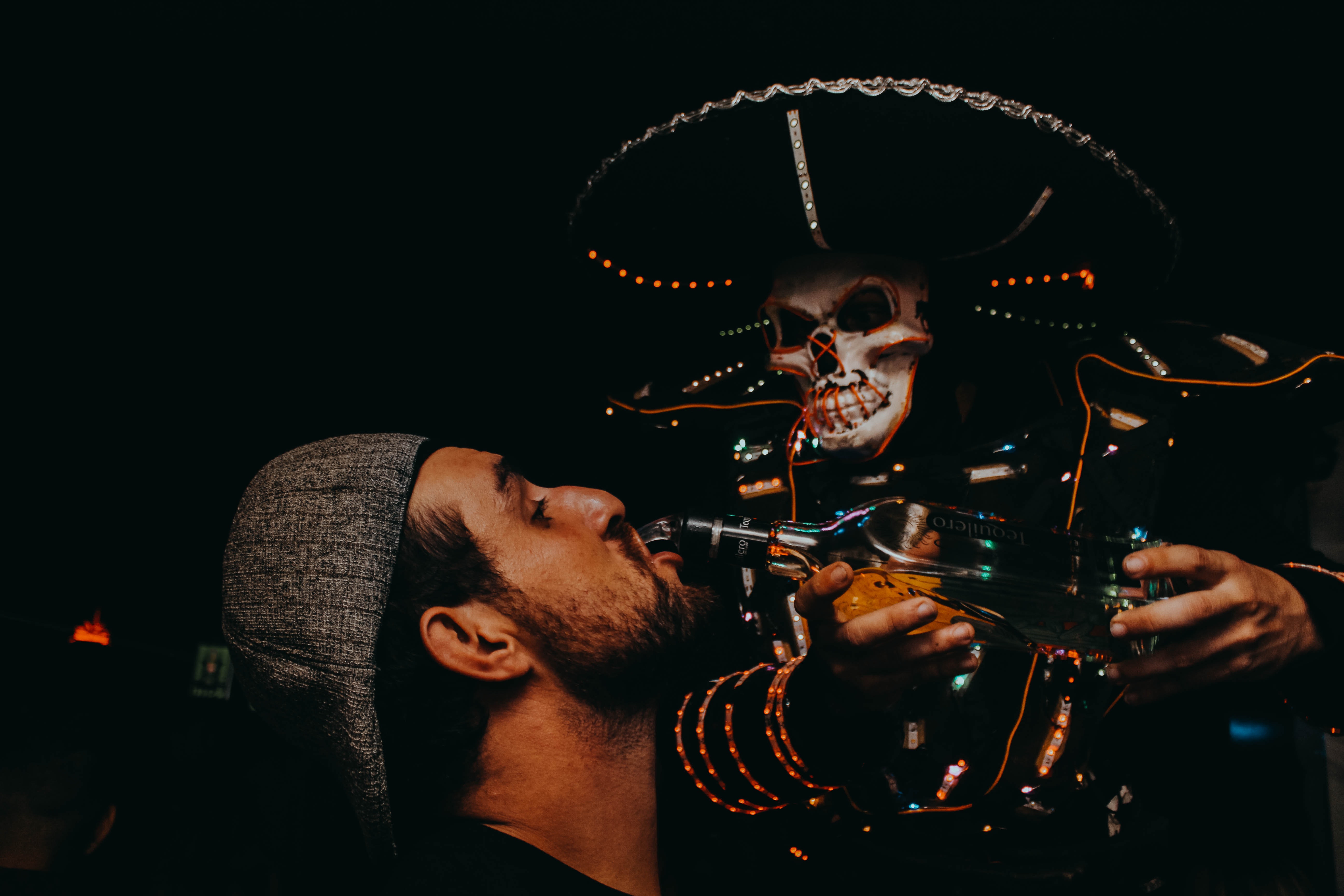 a man drinks alcohol poured into his mouth by a skeleton at a halloween party